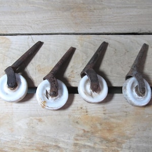 May include: Four antique furniture casters with white ceramic wheels and aged metal hardware. The casters have a conical shape and are arranged on a wooden surface, showcasing their vintage design and potential for restoration projects.