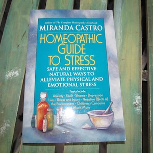 May include: A blue book titled "Homeopathic Guide to Stress" by Miranda Castro. The book cover features a mortar and pestle, bottles of liquid, and the text "Safe and Effective Natural Ways to Alleviate Physical and Emotional Stress".