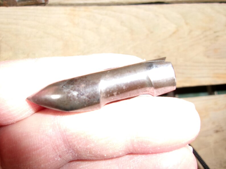 May include: A metallic bullet with a pointed tip and a cylindrical body. The bullet has a silver finish with some darker spots, suggesting age or use. The bullet is held in a hand.