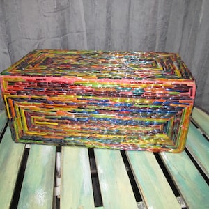 May include: A rectangular box covered in colorful mosaic tiles. The tiles are arranged in a pattern of horizontal and vertical lines, creating a geometric design. The box is made of glass and has a shiny, reflective surface.