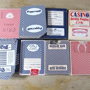 May include: A collection of vintage playing card decks, featuring various designs and casino branding. The decks showcase a range of colors, including red, blue, and white, with text such as "Casino" and "Harolds Club" visible on the packaging.
