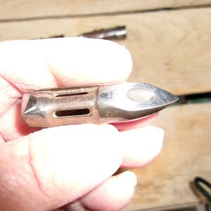May include: A silver-colored metal object with a pointed end and rectangular cutouts. The object is held in a hand, and the background is a wooden surface.