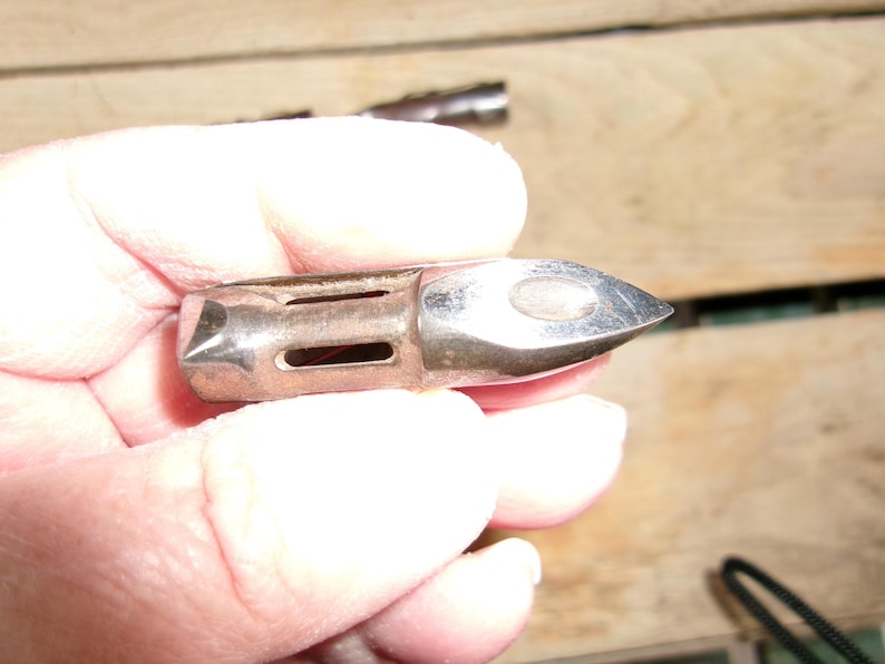 May include: A silver-colored metal object with a pointed end and rectangular cutouts. The object is held in a hand, and the background is a wooden surface.