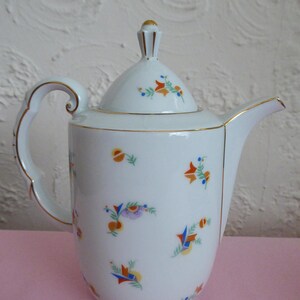 May include: White porcelain coffee pot with a gold trim and a lid. The pot has a floral pattern with orange, blue, and green flowers.