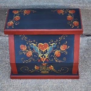May include: A hand-painted wooden box with a hinged lid. The box is painted navy blue with red trim and features floral and bird designs in yellow, red, and blue. The box is rectangular and appears to be a storage container.