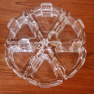May include: A clear glass trinket dish with six sections, shaped like a wheel with spokes. The dish is made of clear glass and has a decorative, textured design.