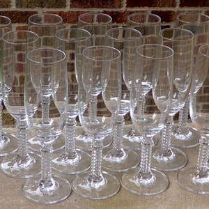 May include: A set of 15 clear glass champagne flutes with a beaded stem design. The flutes are arranged in a staggered pattern on a light gray surface.