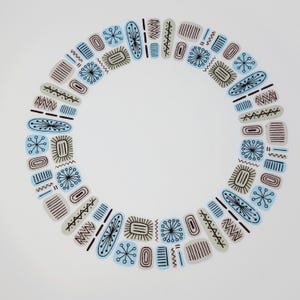 May include: A white plate with a circular design of various shapes and patterns. The design includes light blue, gray, and black elements, such as ovals, rectangles, and starbursts, arranged around the edge of the plate. The center is plain white.