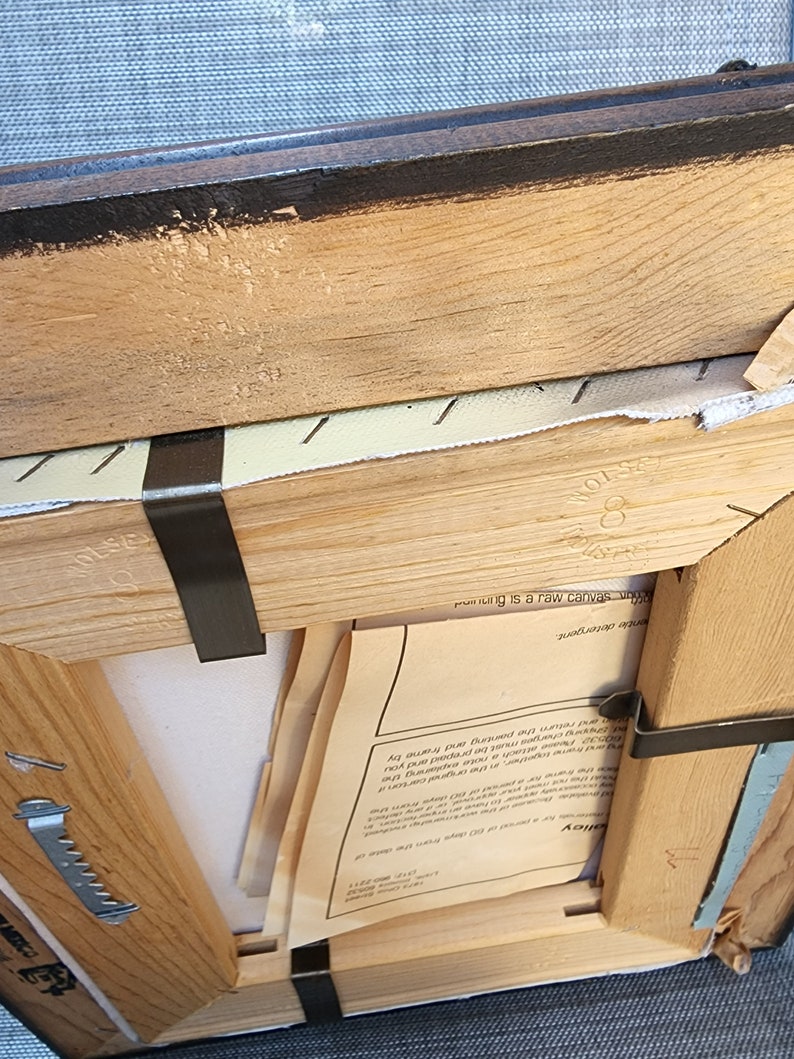 May include: A wooden frame with a canvas inside. The frame is brown and has a black painted edge. The canvas is white and has a piece of paper on it with text that says "This painting is a raw canvas, original art".