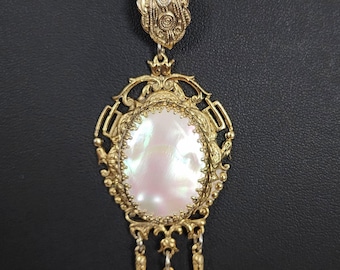 May include: A vintage gold-tone necklace with an ornate pendant. The pendant has a pearlescent oval centre framed by intricate filigree and dangling spear-shaped charms. The chain is a classic link style.