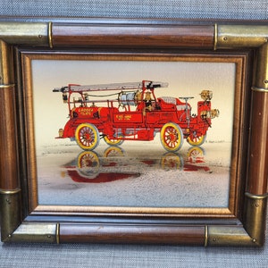 May include: A framed painting of a vintage red fire engine with a ladder, the words "Gaddotta Mains" and "Fire Chief No. 1" on the side. The engine is on a light brown background with a reflection of the engine in the ground.