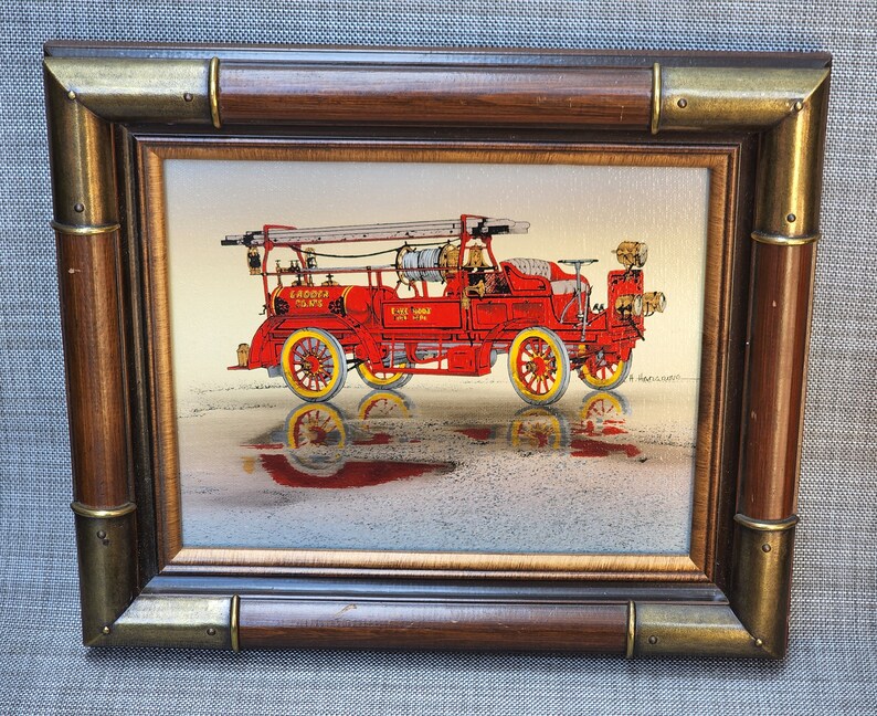 May include: A framed painting of a vintage red fire engine with a ladder, the words "Gaddotta Mains" and "Fire Chief No. 1" on the side. The engine is on a light brown background with a reflection of the engine in the ground.