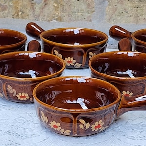 Op de afbeelding: Set van zes bruine keramische ramekins met bloemmotieven. Elk ramekin heeft een handvat en is perfect om individuele porties soep, dip of dessert te serveren.