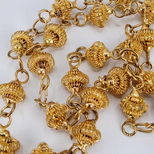 May include: A gold-toned chain necklace featuring multiple spherical beads with a delicate wire-wrapped, cage-like texture. The beads are connected by circular metal links, creating a continuous, repeating pattern throughout the length of the jewelry piece.