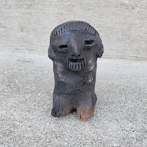 May include: A small, black ceramic figurine of a person with a stylized face and a simple, rounded body.