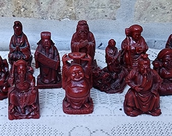 Puede incluir: Un conjunto de 12 figuras de madera roja que representan a varios personajes de la mitología china. Las figuras están todas en posición sentada y están intrincadamente talladas con detalles.
