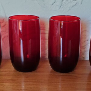 May include: Four red glass tumblers with a dark red base. The glasses are clear and have a smooth, rounded shape.