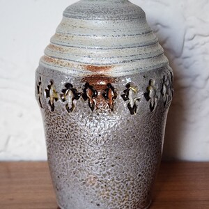 May include: A white ceramic vase with a textured surface and brown accents. The vase has a rounded shape and a wide opening at the top.