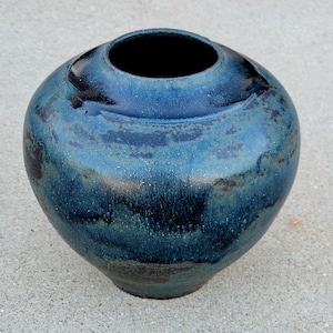 May include: A handcrafted ceramic vase with a rounded body and a wide opening. The vase features a blend of blue and teal hues with dark accents, creating a textured, glazed finish. The pottery is suitable for home decor.