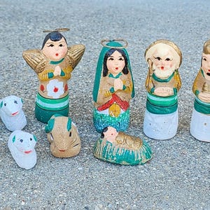 May include: A collection of hand-painted, vintage Christmas nativity figurines. The figures include Mary, Joseph, baby Jesus, angels, and wise men. The figurines are painted in various colors, including green, gold, and white.