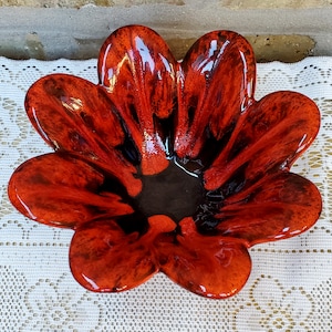 May include: A red and black ceramic flower-shaped bowl with a glossy finish. The bowl has a deep center and five petals.