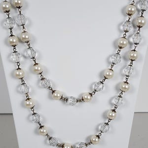 May include: Two-strand necklace featuring faux pearls and clear, faceted beads. The beads are strung on a dark metal chain. The necklace is displayed on a white mannequin bust.