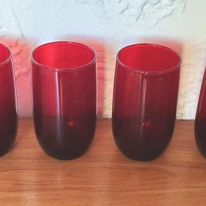 May include: Set of four red glass tumblers with a gradient from red to dark red. The glasses are clear and have a smooth, rounded shape.