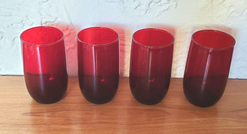 May include: Set of four red glass tumblers with a gradient from red to dark red. The glasses are clear and have a smooth, rounded shape.