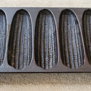 May include: A cast iron cornbread pan with eight individual molds. The pan is dark gray and has a textured surface.