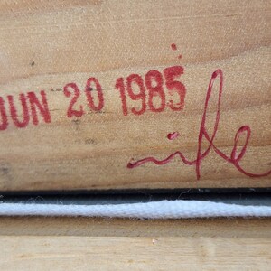 May include: Close-up of a wooden surface with a red stamp that reads "JUN 20 1985" and a red signature that reads "mike".