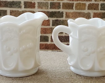 May include: A set of two white milk glass creamer and sugar bowls with a scalloped rim and embossed floral design.