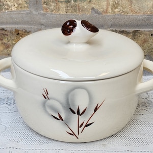 May include: White ceramic casserole dish with a lid. The lid has a brown and white knob in the shape of a flower. The dish has a brown and white floral design.