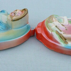 May include: Two ceramic wall plaques depicting women in a reclining pose. The plaques are painted in a pastel color scheme with blue, pink, and green accents. The women are wearing dresses and have long hair.