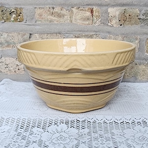 May include: A large, yellow ceramic mixing bowl with brown stripes around the rim. The bowl has a textured, wavy design.