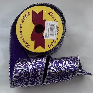 May include: A roll of purple Renaissance 2000 ribbon with a silver floral pattern. The ribbon is 2.5 inches wide and has a metallic silver edge. The spool has a yellow label with the text "Renaissance 2000".