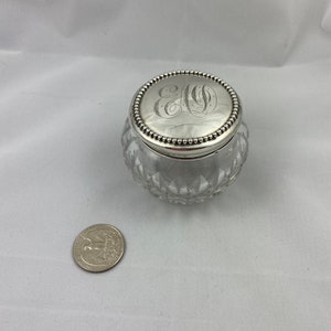 May include: A clear glass jar with a silver lid. The lid has a beaded edge and an engraved monogram.