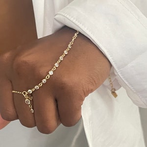 Könnte beinhalten: Ein goldenes Kettenarmband mit kleinen, klaren Steinen. Das Armband hat einen Anhänger mit einem kleinen, klaren Stein.