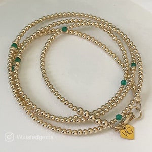 May include: Three gold bracelets with green beads. The bracelets are layered on top of each other and have a clasp with the initials "WG" on it.