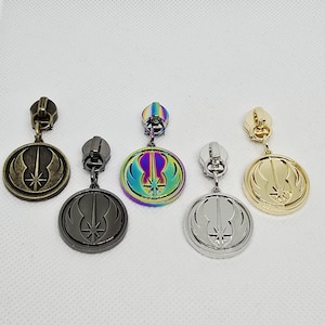 May include: Five circular zipper pulls featuring a Jedi Order symbol. The set includes finishes in antique bronze, matte black, iridescent rainbow, polished silver, and polished gold. Each metal charm is attached to a standard zipper slider mechanism.