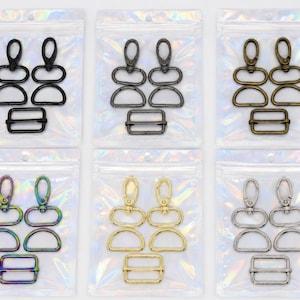 May include: Six sets of metal hardware components, each contained in a clear iridescent plastic bag. Every set includes two swivel lobster clasps, two D-rings, and one rectangular slider buckle, available in black, gunmetal, bronze, rainbow, gold, and silver.
