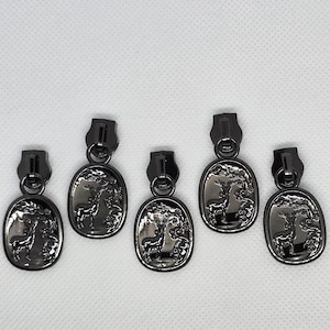 May include: Five black metal zipper pulls with a deer design. Each pull features a detailed deer standing in a forest scene.