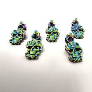 May include: Five iridescent zipper pulls with a skull design. The skulls are detailed with a snake and have a rainbow finish.