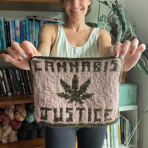 Puede incluir: Un cuadrado tejido con las palabras "CANNABIS JUSTICE" y un diseño de hoja de cannabis. El texto y la hoja son de color verde oscuro sobre un fondo rosa, con un borde verde oscuro. El artículo está hecho a mano.