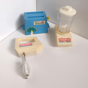 May include: A collection of vintage toy kitchen appliances, including a blue plastic toaster with the word "Toaster", a blender, and a hand mixer. The blender and mixer are off-white with the text "Kiddy-Magic" and "Kiddy-Matic".
