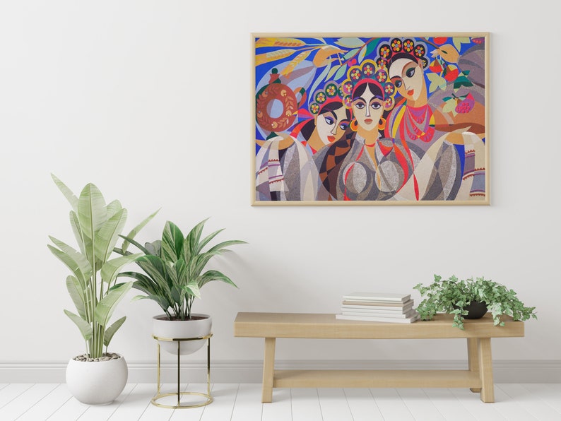 May include: A framed painting depicting three women wearing colourful clothing and floral headbands. The women are standing in front of a blue background with green leaves and flowers. The painting is in a wooden frame.