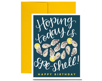 May include: A blue card with the text "Hoping today is spe-shell!" in white cursive writing. The card is decorated with illustrations of oysters and lemons. The text "Happy Birthday" is printed in white at the bottom of the card.