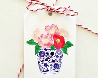 May include: A white gift tag with a blue and white floral design. The tag has the words "To:" and "From:" written on it.