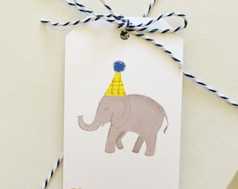May include: A white gift tag with a gray elephant wearing a yellow and blue party hat. The tag has the words "TO:" and "FROM:" printed on it.