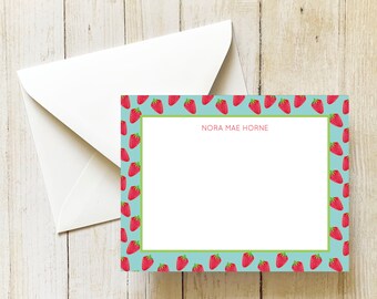 May include: A light blue stationery card with a white border and a repeating pattern of red strawberries. The card has a blank space for writing and the name "Nora Mae Horne" printed at the top.