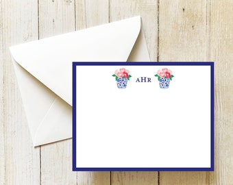 May include: White stationery set featuring a navy blue border and floral design. The stationery includes a card with two blue and white vases filled with pink flowers, and the initials "AHR". An envelope is also included.